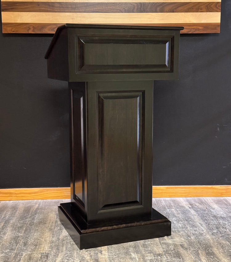 Dark wooden podium against a black wall with a wooden panel above.