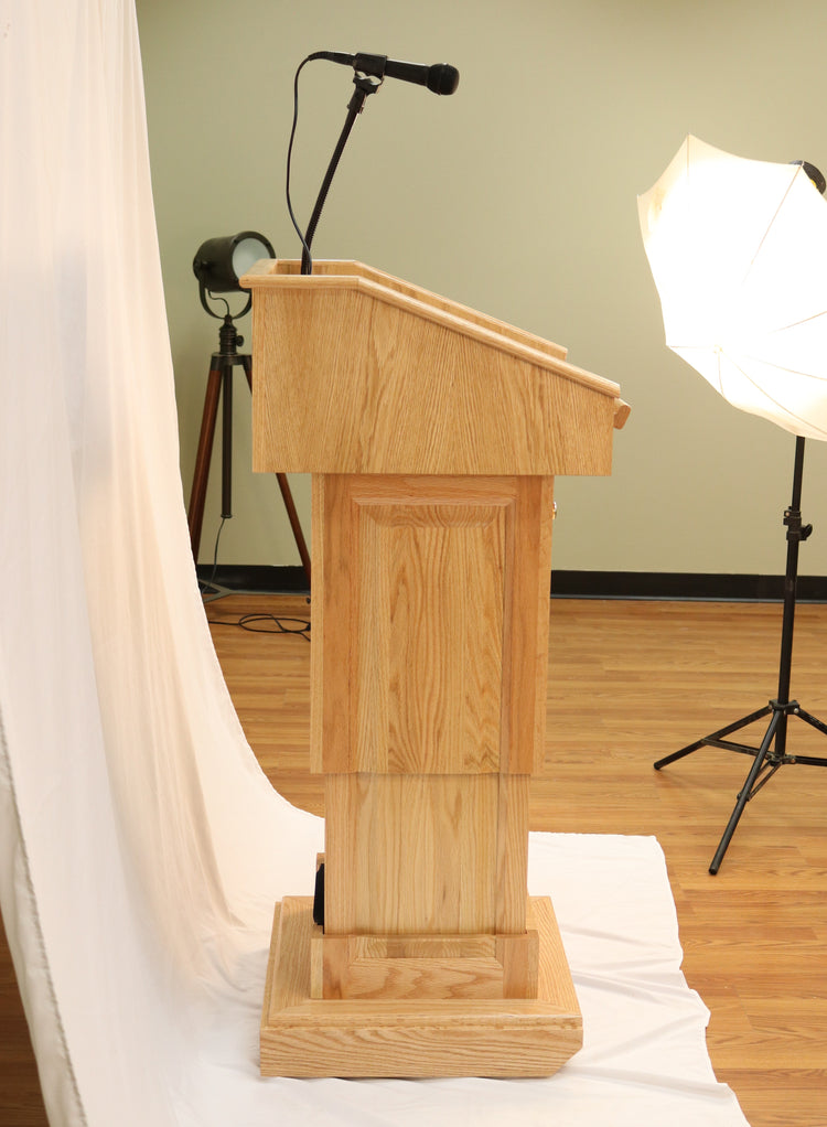 The Counselor Evolution Lift™ lectern, handcrafted from oak wood, features adjustable height, built-in sound system, and mobility casters.