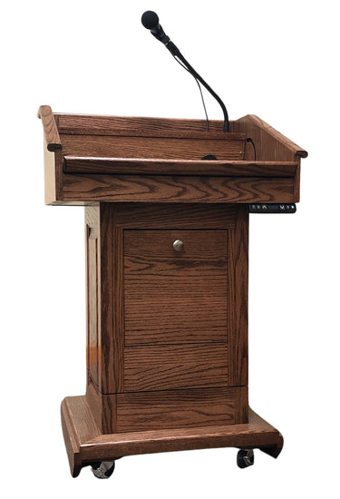 The Counselor Evolution Lift™ lectern, handcrafted from oak wood, features adjustable height, built-in sound system, and mobility casters.