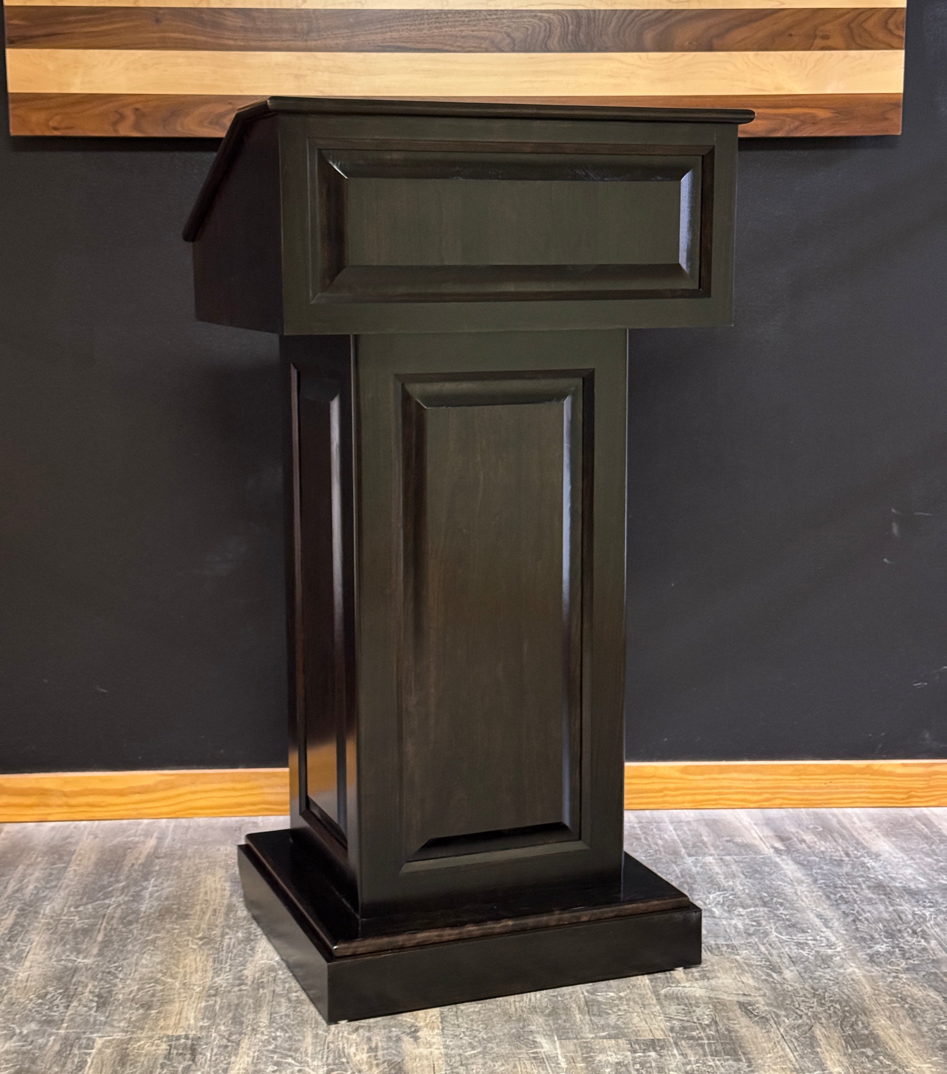 Dark wooden podium against a black wall with a wooden panel above.