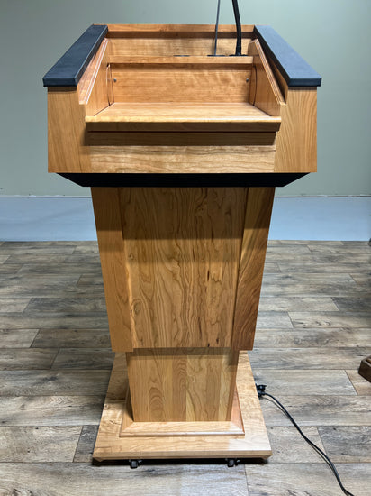 Height-adjustable wooden podium with magnetic front for logos, leather handrails, and a drop-down work surface for presentations.