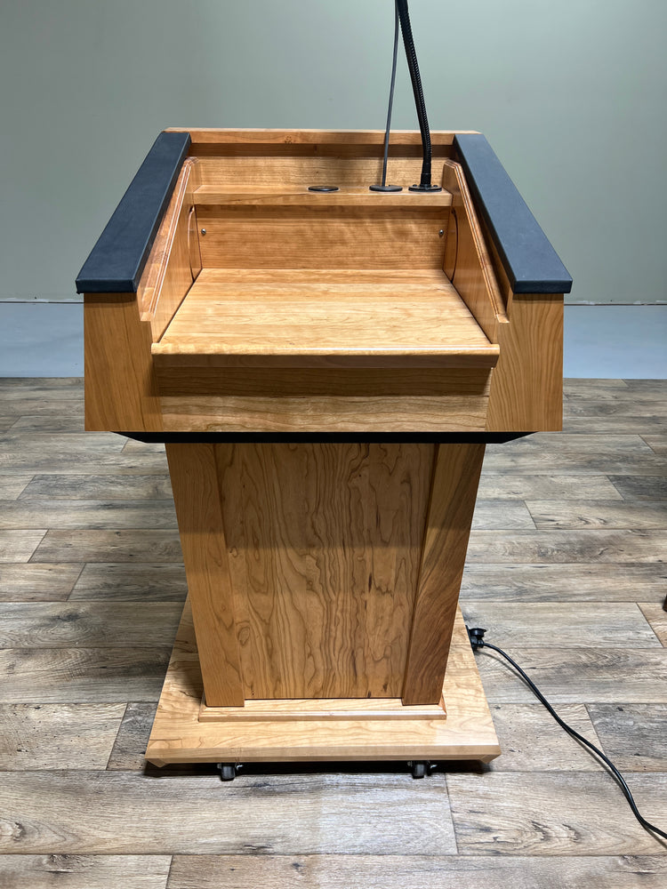 Height-adjustable wooden podium with magnetic front for logos, leather handrails, and a drop-down work surface for presentations.