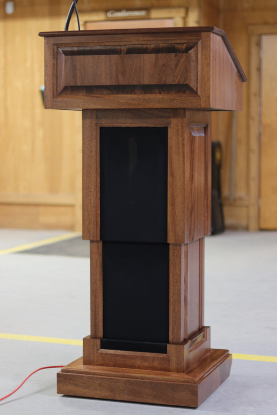 The Counselor Evolution Lift™ podium, handcrafted from mahogany wood, features power adjustable height, built-in sound system, and casters.