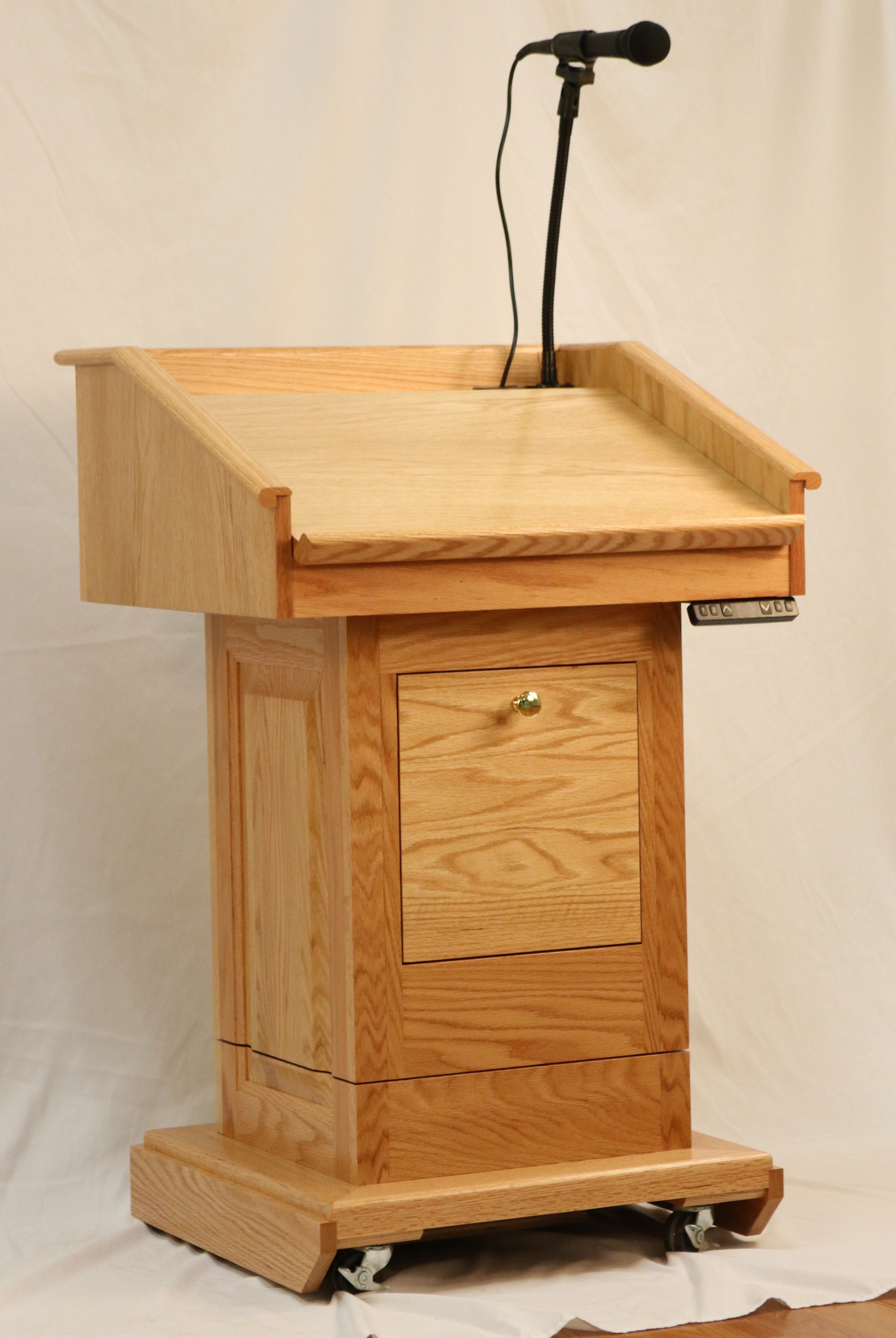 The Counselor Evolution Lift™ lectern, handcrafted from oak wood, features adjustable height, built-in sound system, and mobility casters.