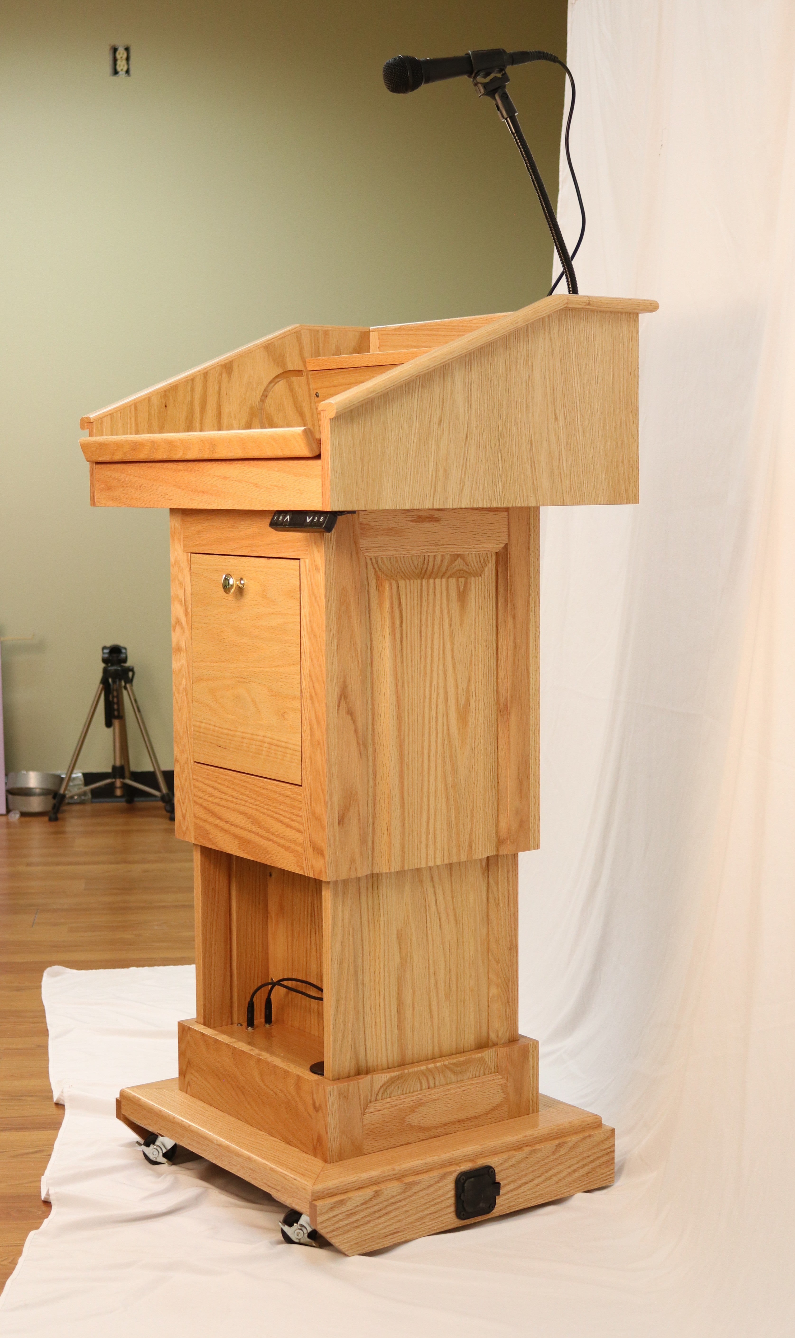 The Counselor Evolution Lift™ lectern, handcrafted from oak wood, features adjustable height, built-in sound system, and mobility casters.