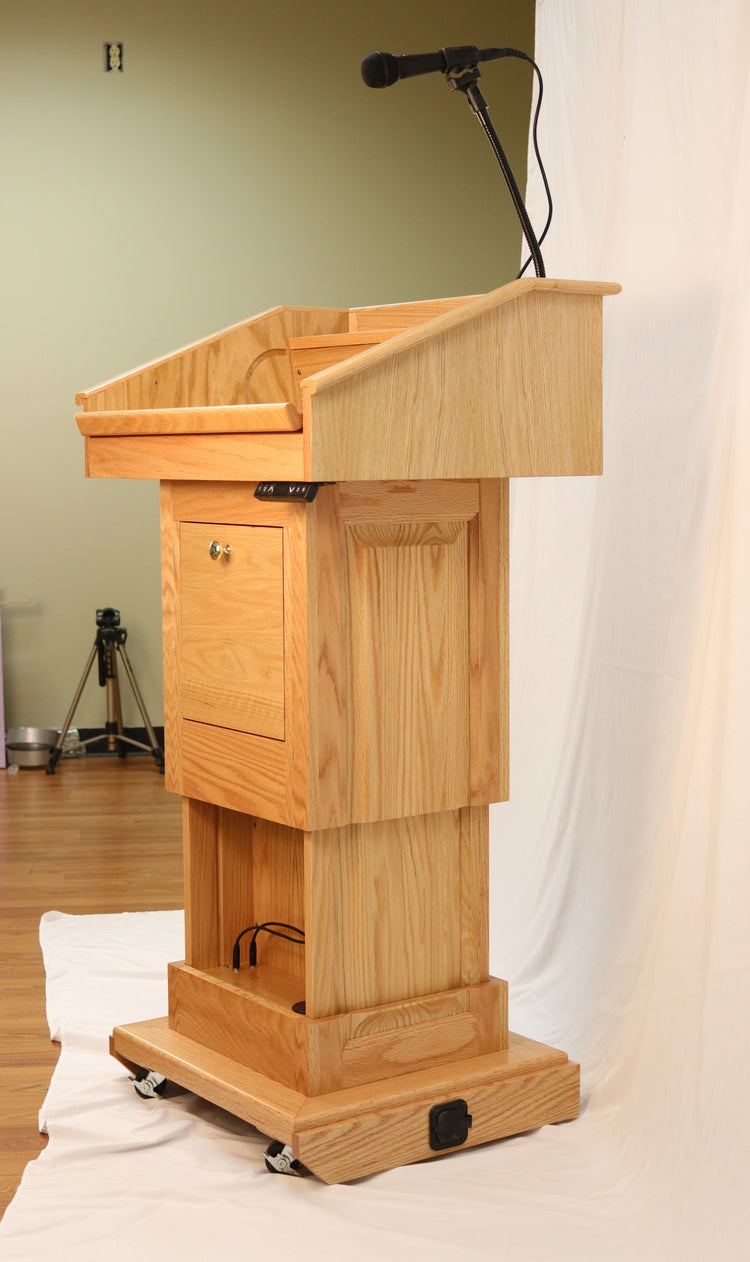 The Counselor Evolution Lift™ lectern, handcrafted from oak wood, features adjustable height, built-in sound system, and mobility casters.