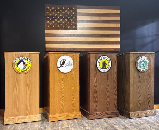 Four wooden podiums with emblems in front of an American flag on a dark wall.
