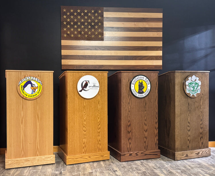 Four wooden podiums with emblems in front of an American flag on a dark wall.